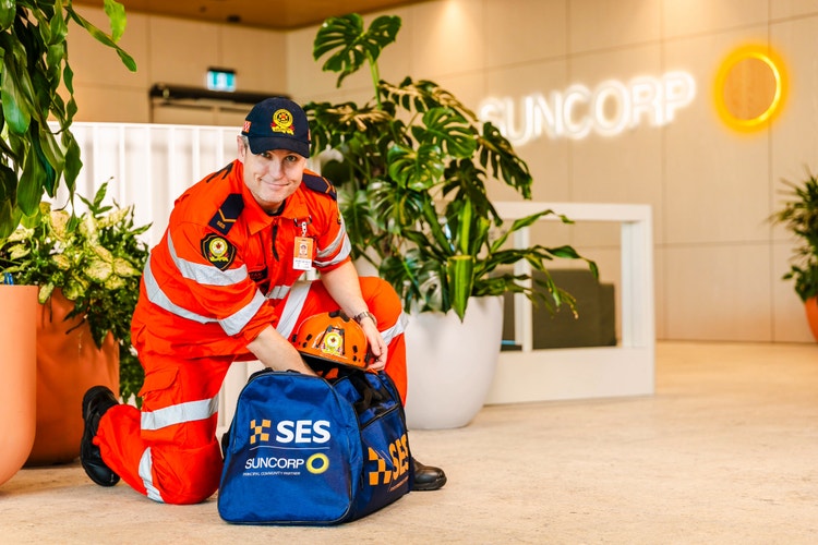 SES volunteer kneeling and reaching into SES bag with Suncorp logo visible in background