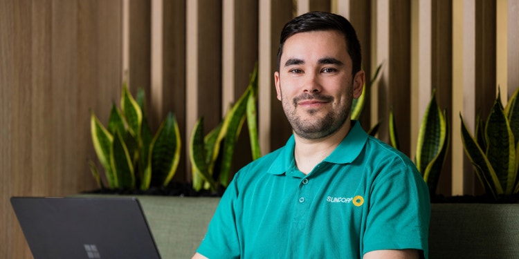 man wearing green suncorp polo sitting in at desk with computer