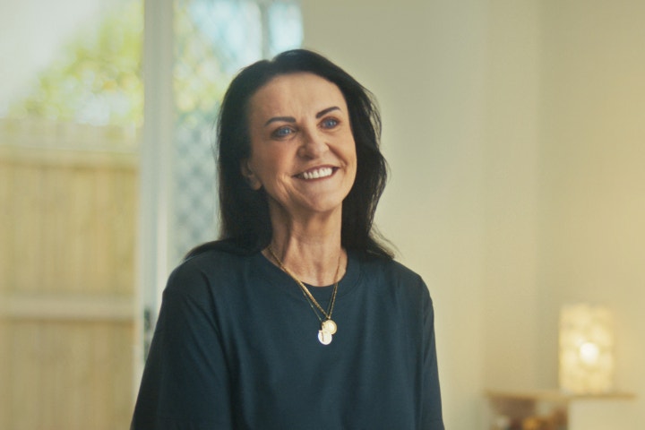 Woman wearing green top sitting in brightly it living room smiling at camera