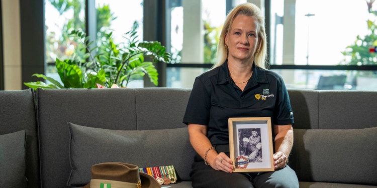 Woman sitting on couch holding picture frame with black and white image of her uncle in uniform. On the couch are some medals and an army hat.