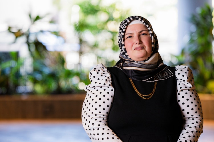 Woman wearing black dress with white dots and headscarf standing in front of city garden.