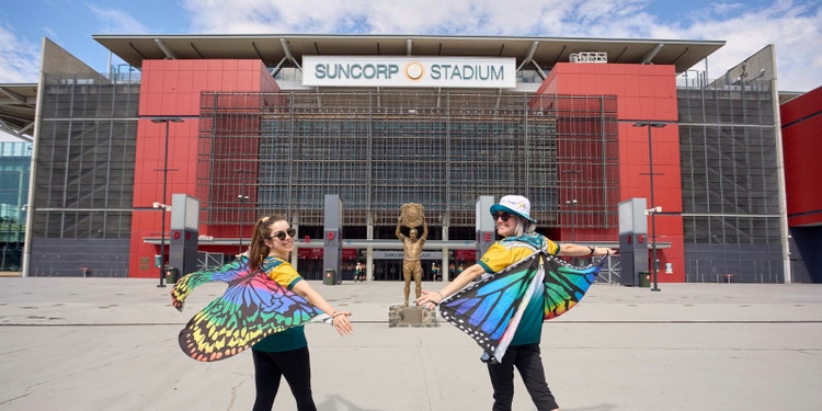 Two women holding up rainbow butterfly wings outside Suncorp stadium
