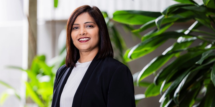 brown-haired person wearing black blazer standing in front of office garden