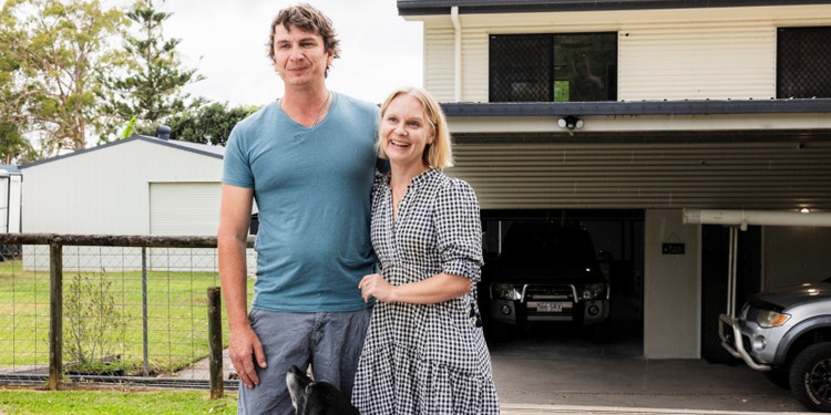 young couple standing outside their home smiling with dog