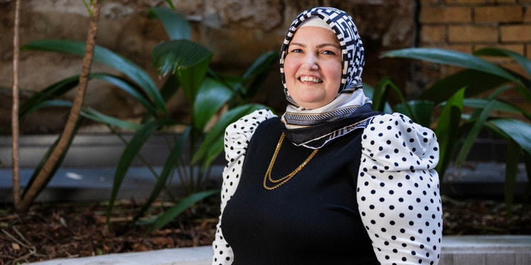 Woman wearing black dress with white dots and headscarf standing in front of city garden.