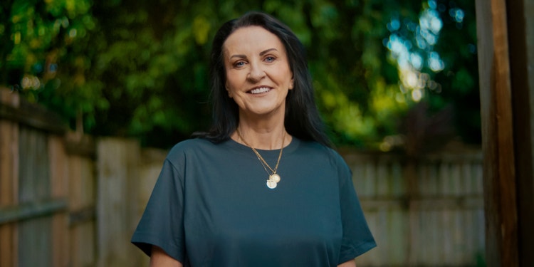 Woman wearing green top standing in driveway smiling at camera