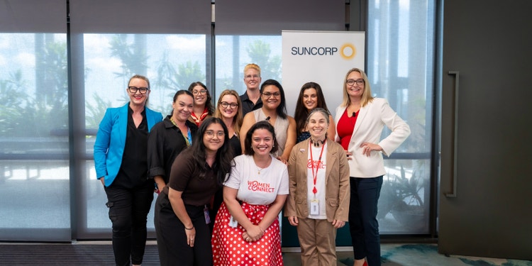 group of women standing in front of suncorp banner and smiling