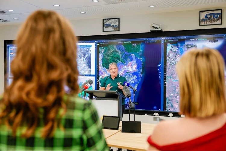 Woman standing in front of large screens giving talk to audience.