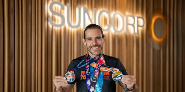 man holding medals hanging from his neck with suncorp sign behind him