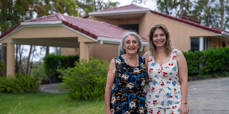 elderly woman and adult daughter hugging and smiling outside home