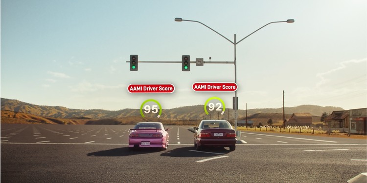 two cars lined up on road before green light with aami driver score displaying in the air above cars