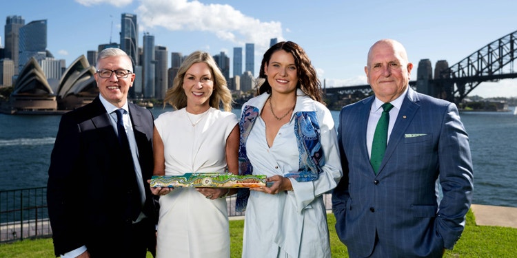 two men and two women in formal wear standing on lawn in front of Sydney opera house and harbour bridge