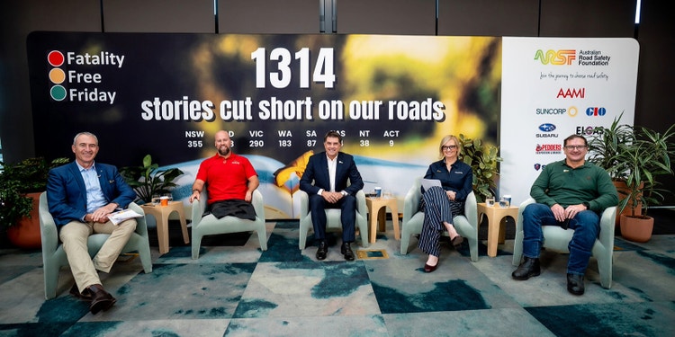 Panellists smiling at camera with billboard showing road toll statistics behind them.